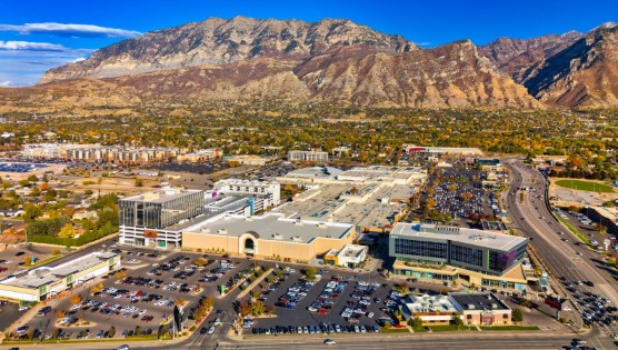 Aerial of Orem, Utah during autumn, featuring the University Place mall in the foreground, and various residential neighborhoods and the Wasatch Range mountains in the background.