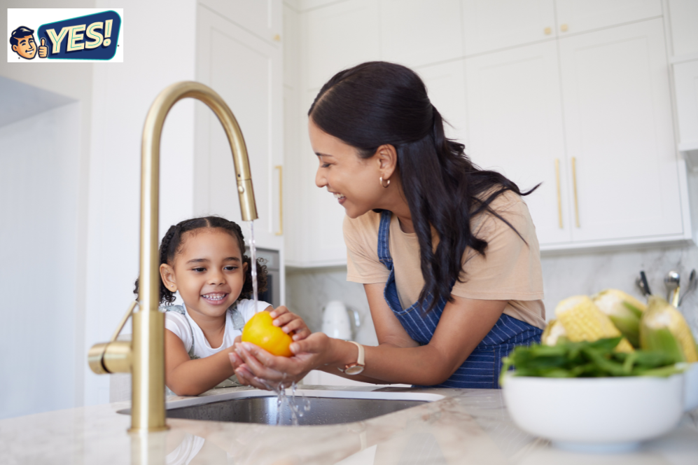 Mother and daughter smiling, washing a yellow bell pepper at the kitchen sink with purified water from the tap.