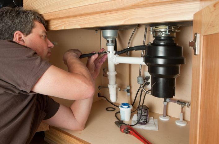 YES! technician in Las Vegas, repairing garbage disposal under sink with tools.