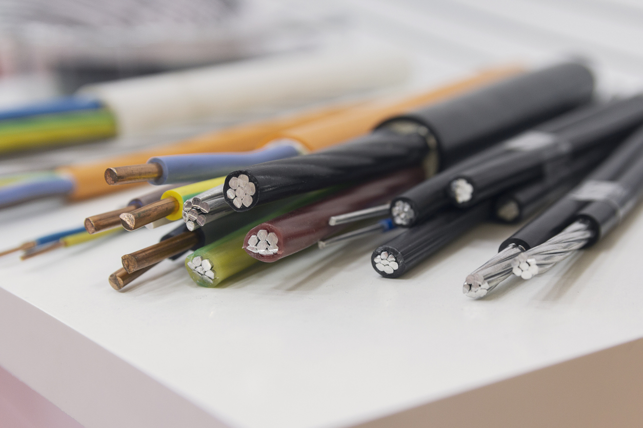 Close-up of assorted electrical cables with stripped ends, showing silver-colored aluminum conductors beside reddish copper wires to illustrate how to identify aluminum wiring.