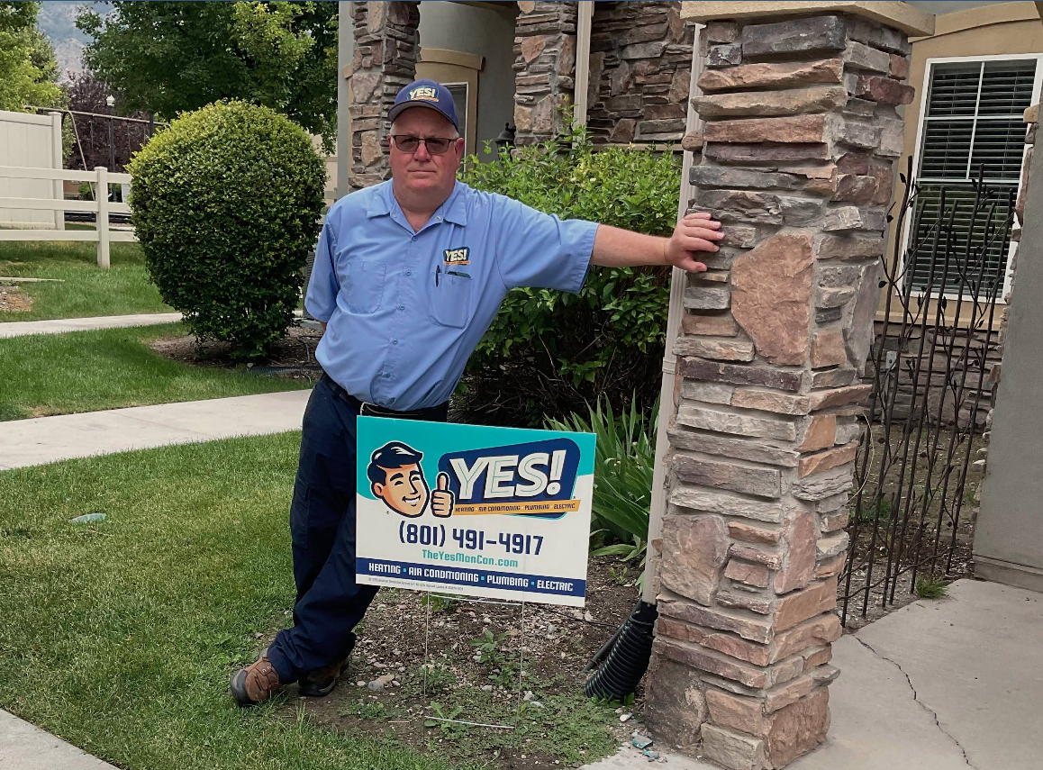 Plumbing technician in Sandy, UT, at a residential home outside with YES! sign.